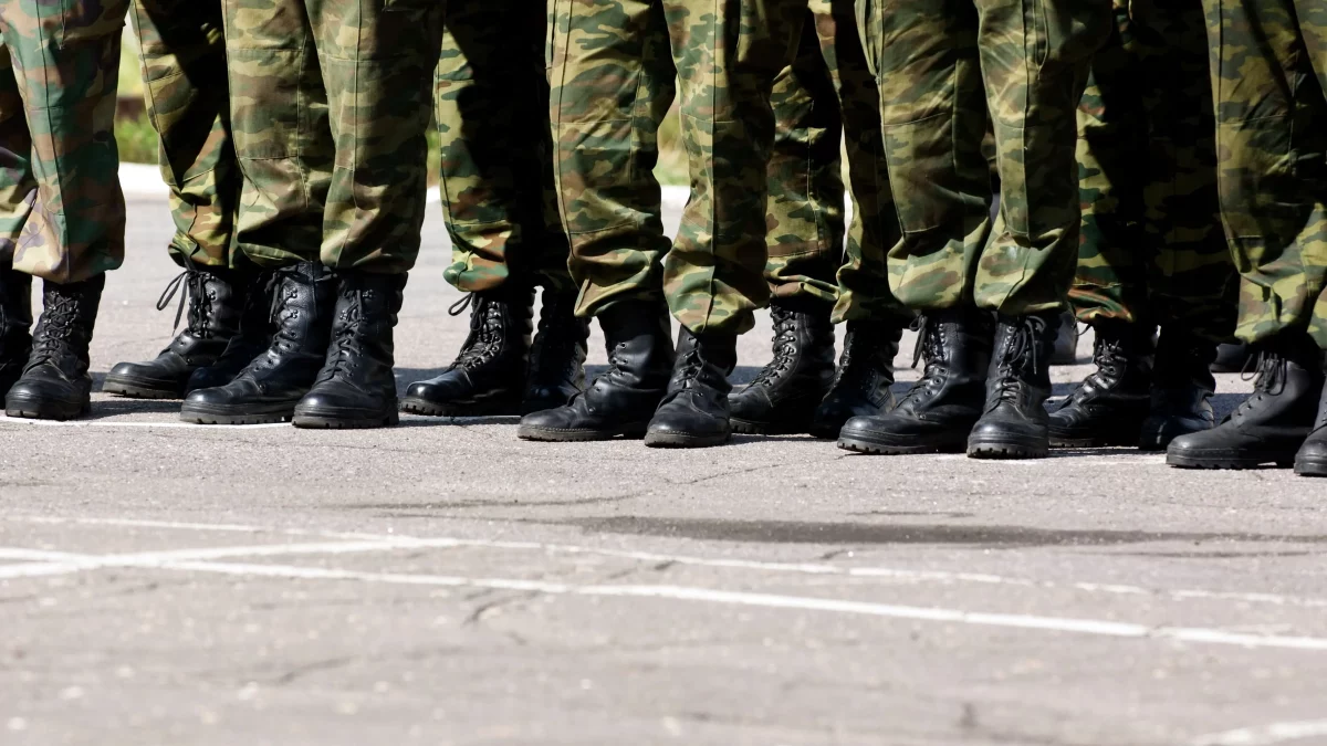 Militares enfileirados com uniformes camuflados e botas pretas, representando cobranças administrativas relacionadas à devolução de pensão militar.