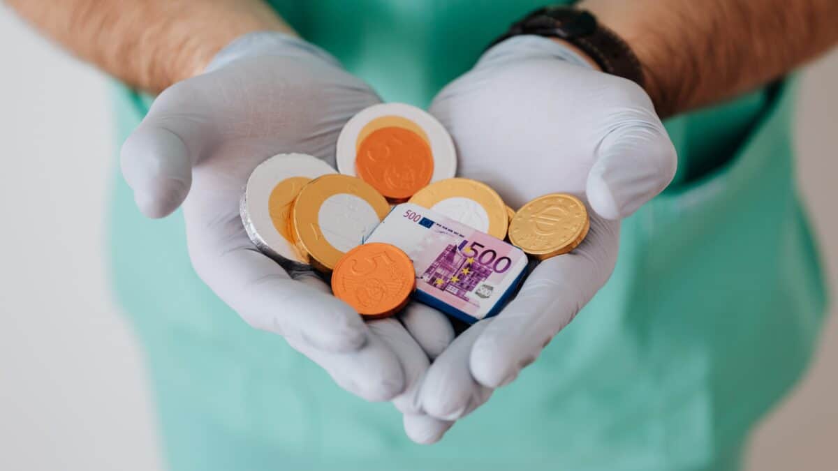 imagem aproximada das mãos de um profissional da saúde, vestindo luvas cirúrgicas e segurando algumas moedas referindo-se ao reajuste do plano de saúde em 2022