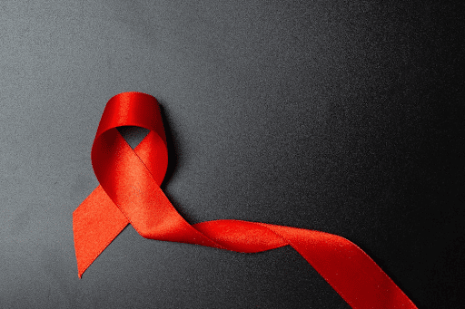 Imagem de um fundo escuro com uma fita vermelha para simbolizar portador de HIV